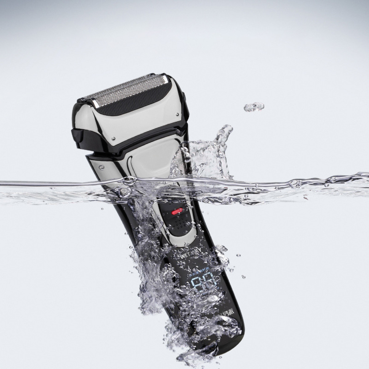 Elektrischer Rasierer taucht in Wasser, mit Spritzern und Blasen.
