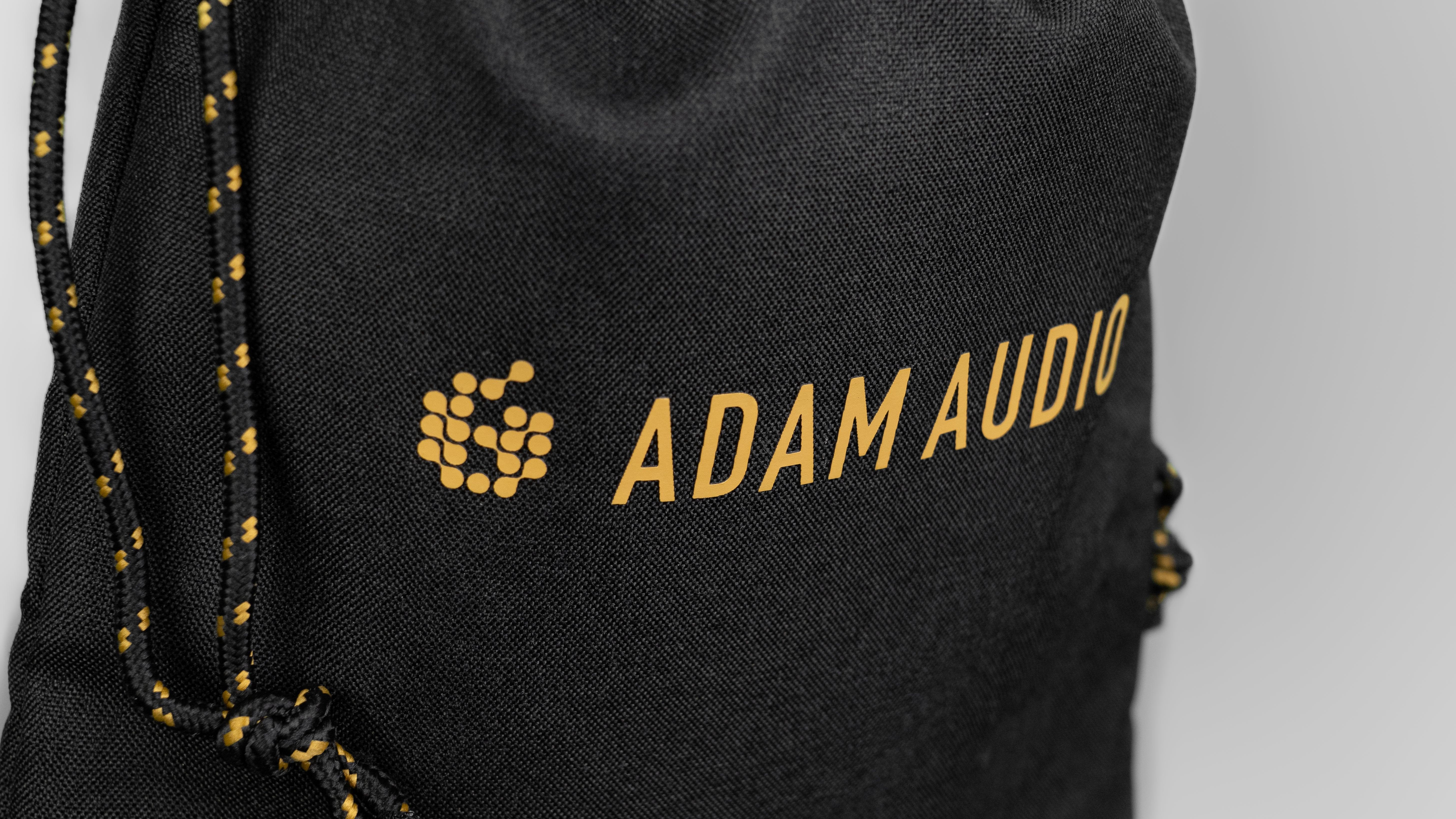 Czarna torba z żółtym logo Adam Audio i sznurkiem.