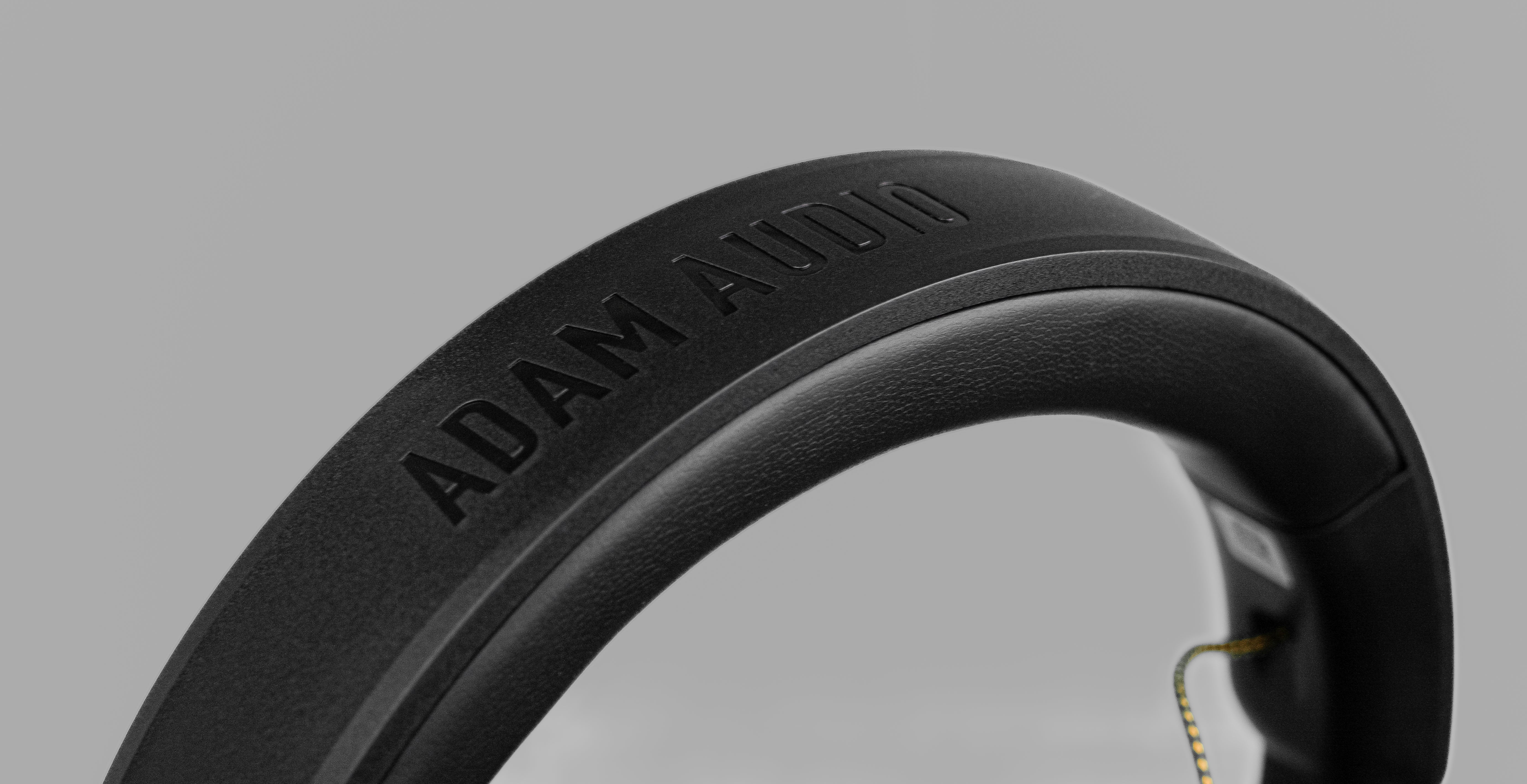 Czarna opaska słuchawek z wytłoczonym napisem ADAM AUDIO na szarym tle.