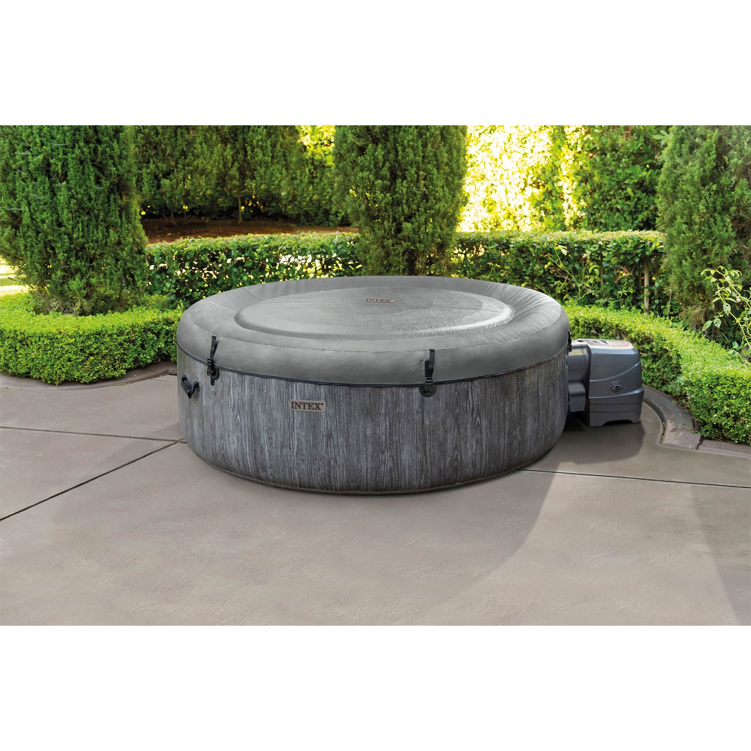 Aufblasbarer Whirlpool mit Holzmaserung auf einer Betonoberfläche, umgeben von grünen Büschen.