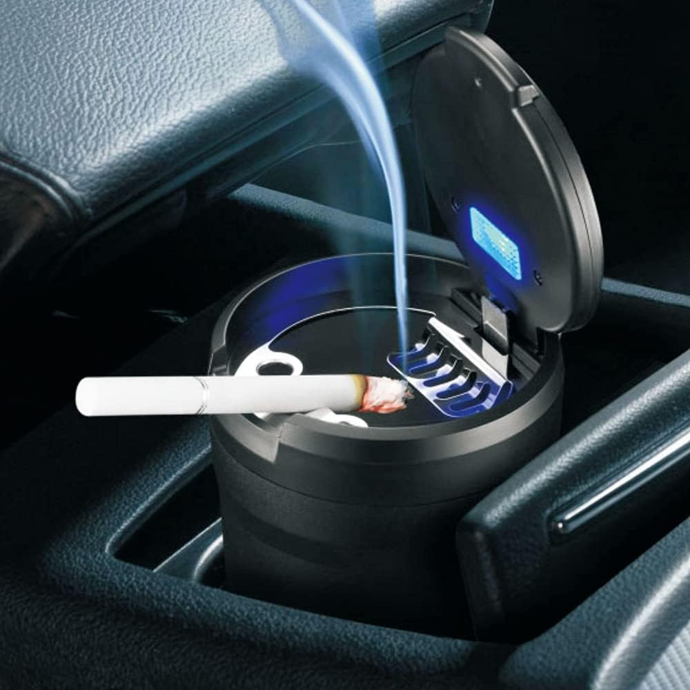 Eine brennende Zigarette liegt in einem Auto-Aschenbecher mit blauer LED. Rauch steigt auf.
