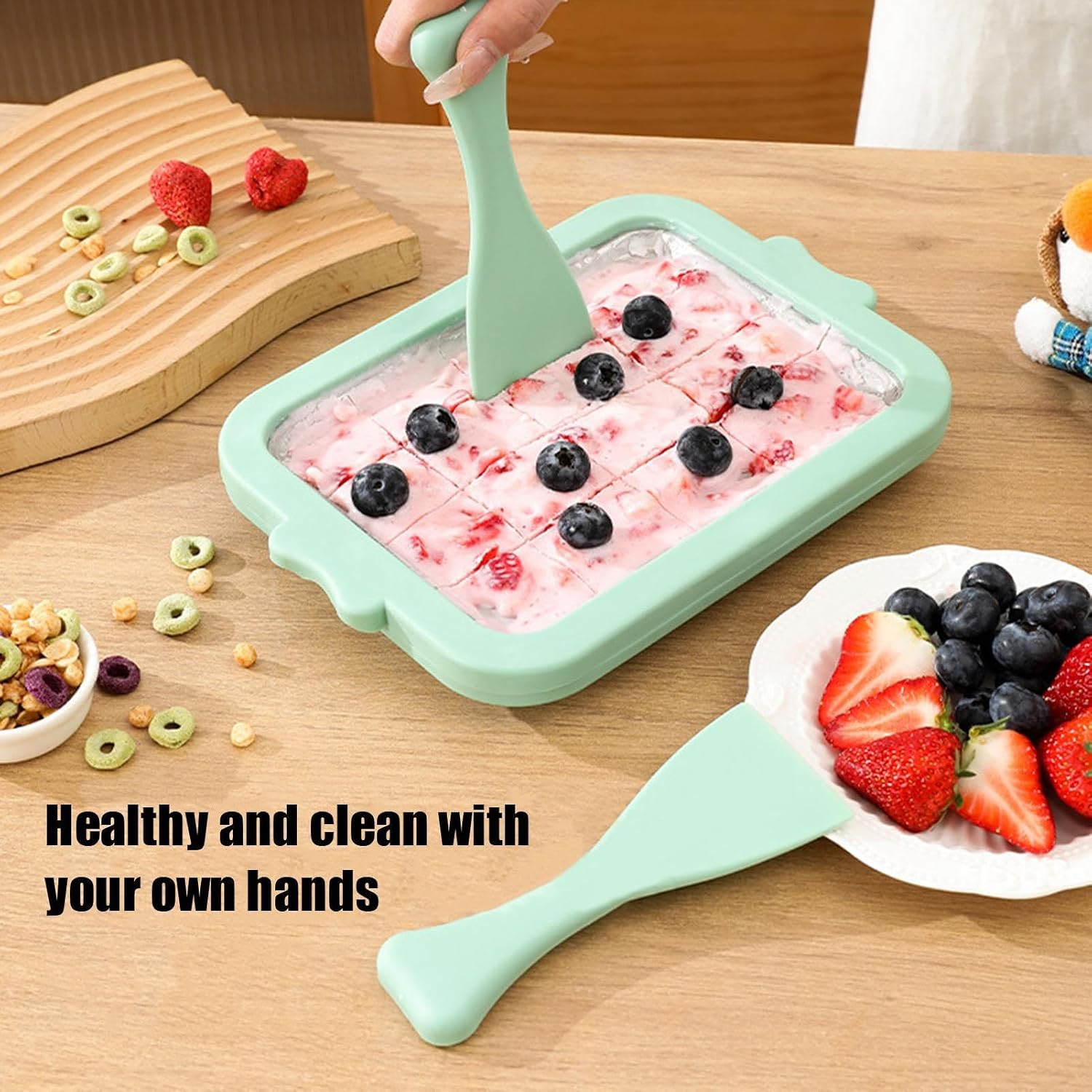 Minzfarbener Eishersteller mit Blaubeeren, Erdbeeren und Müsli auf Holztisch.