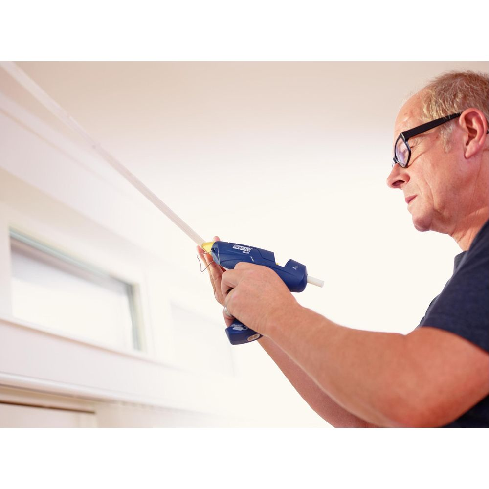 Uomo con pistola per colla che fissa una striscia di legno al muro.