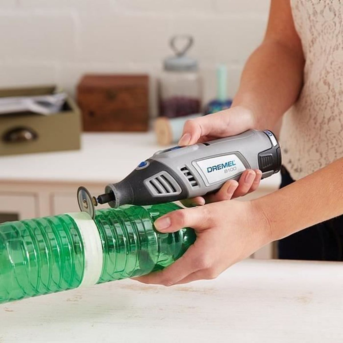 Le mani usano uno strumento Dremel per tagliare una bottiglia di plastica verde con nastro bianco.