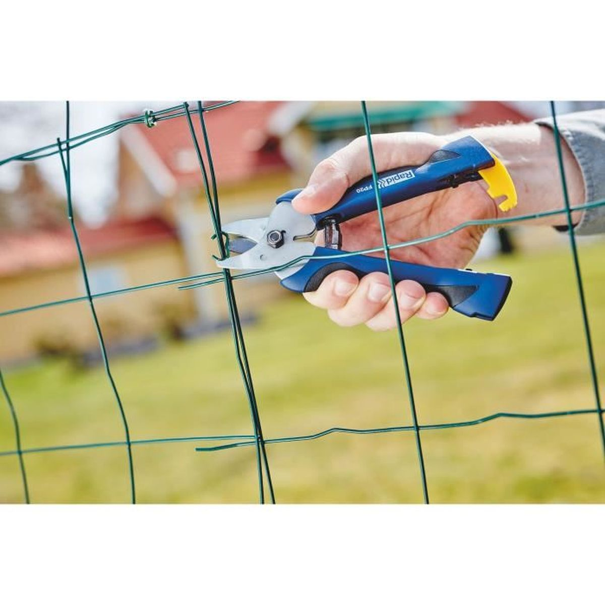 Una mano usa una tronchese blu per tagliare una recinzione di filo verde.