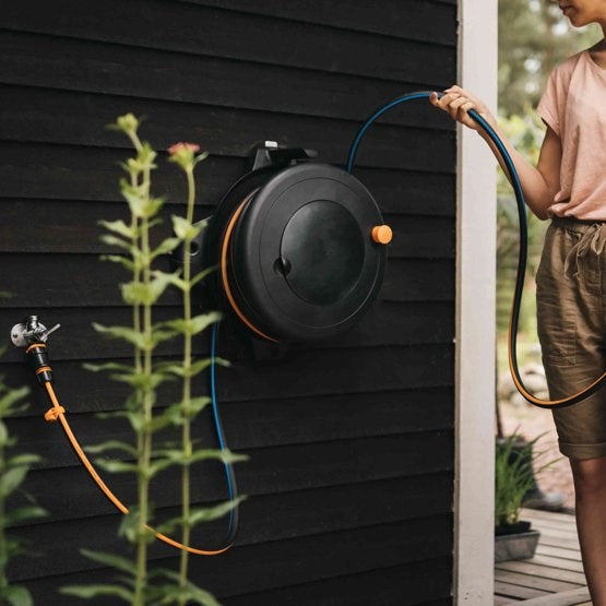 Una persona tiene un tubo da giardino srotolato da un avvolgitubo nero su una parete di legno.