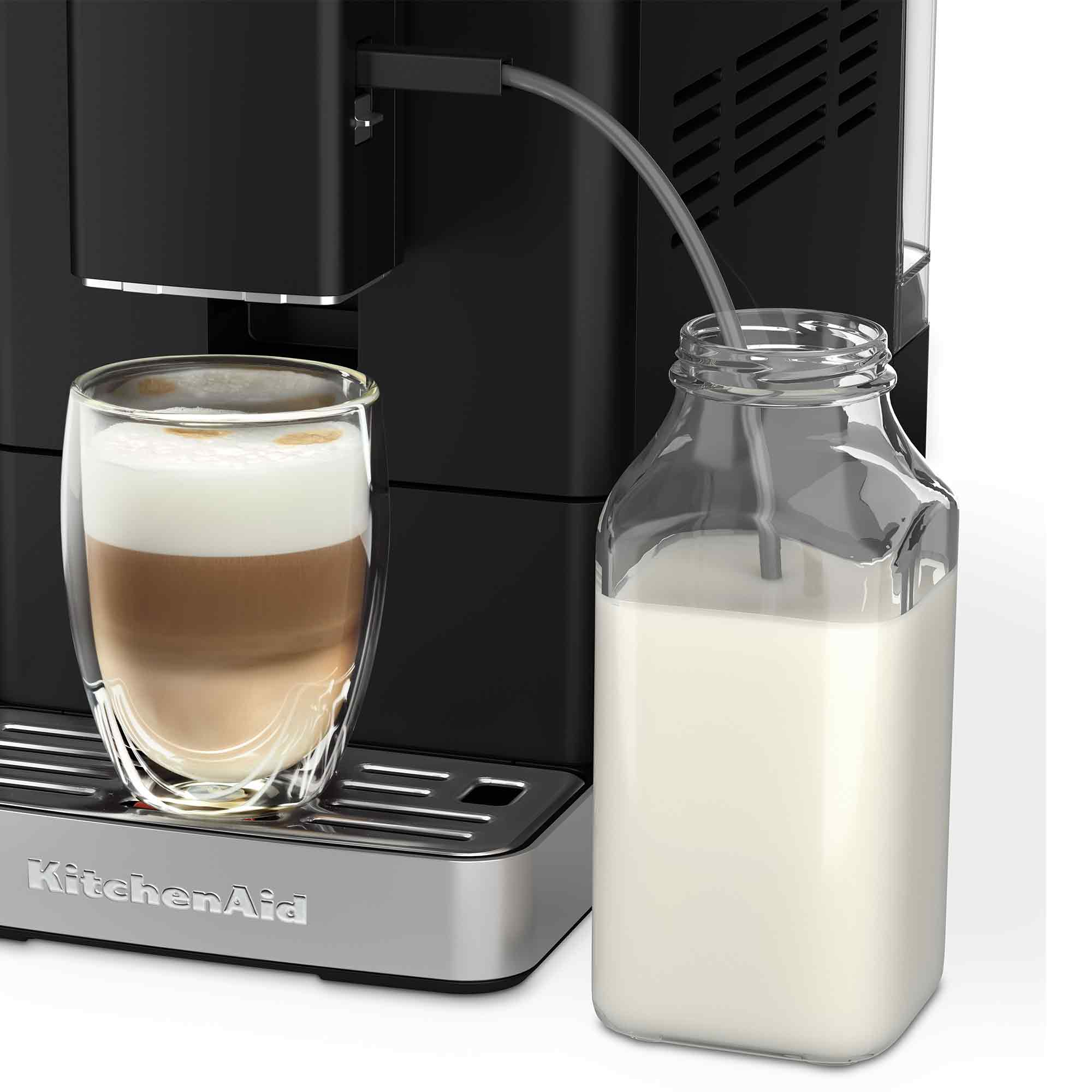 Bir KitchenAid kahve makinesi, süt sürahisinin yanında bir bardakta katmanlı latte hazırlıyor.