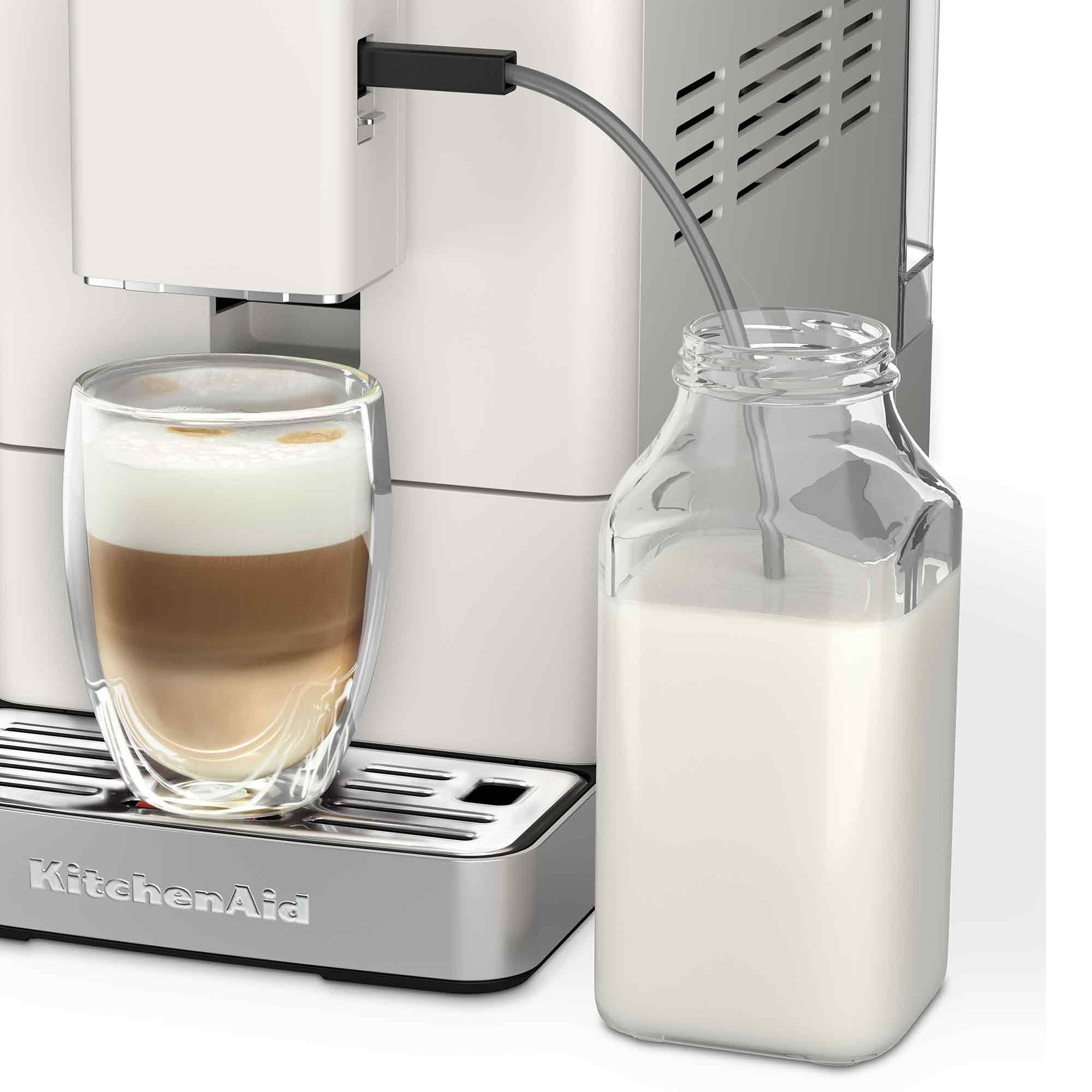 Latte bardaklı ve süt şişeli beyaz kahve makinesi.