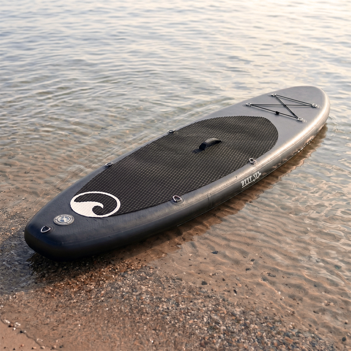 Ein dunkelgraues Schlauchboot-Paddleboard liegt am Ufer im Wasser.