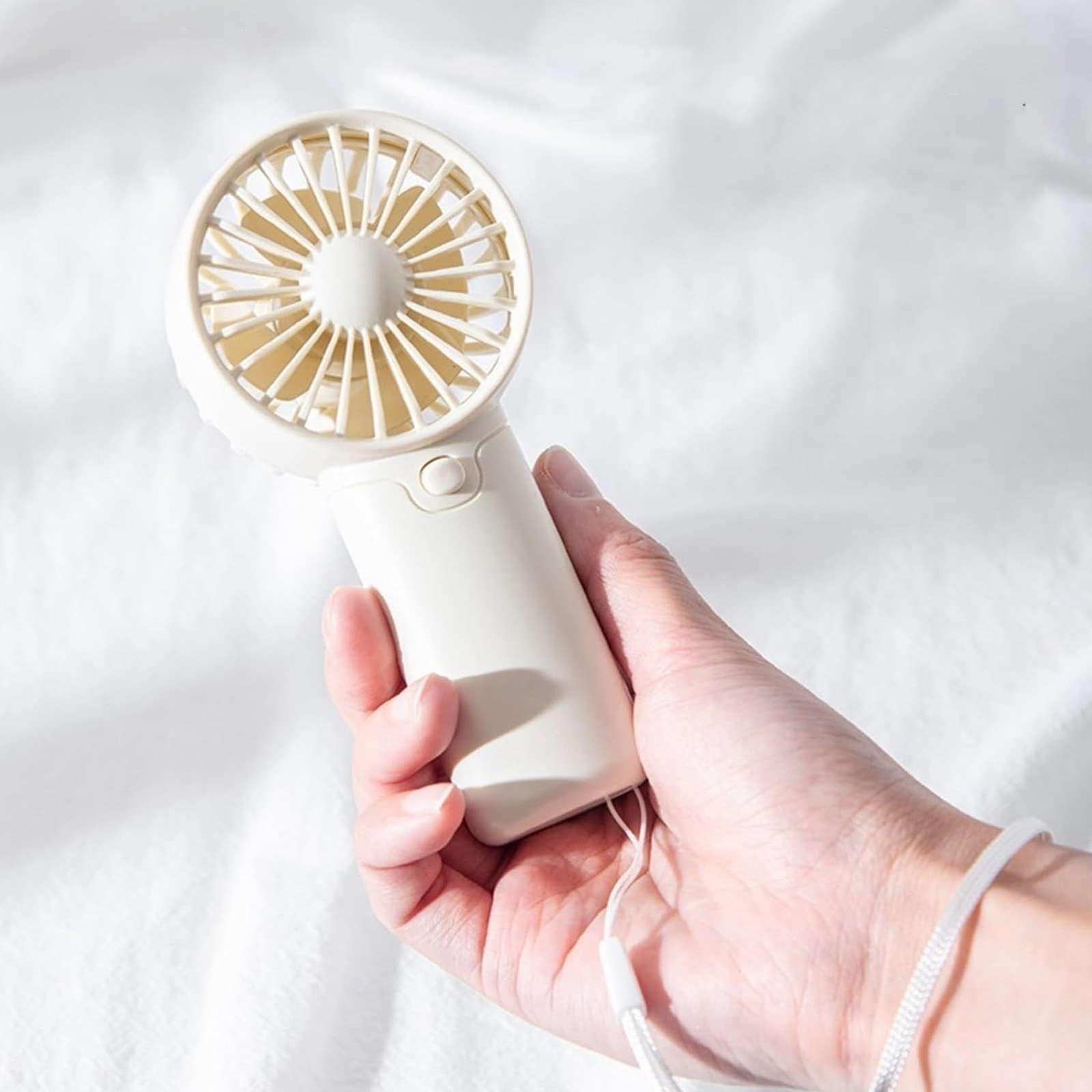 Eine Hand hält einen kleinen, cremefarbenen Handventilator mit Schnur.