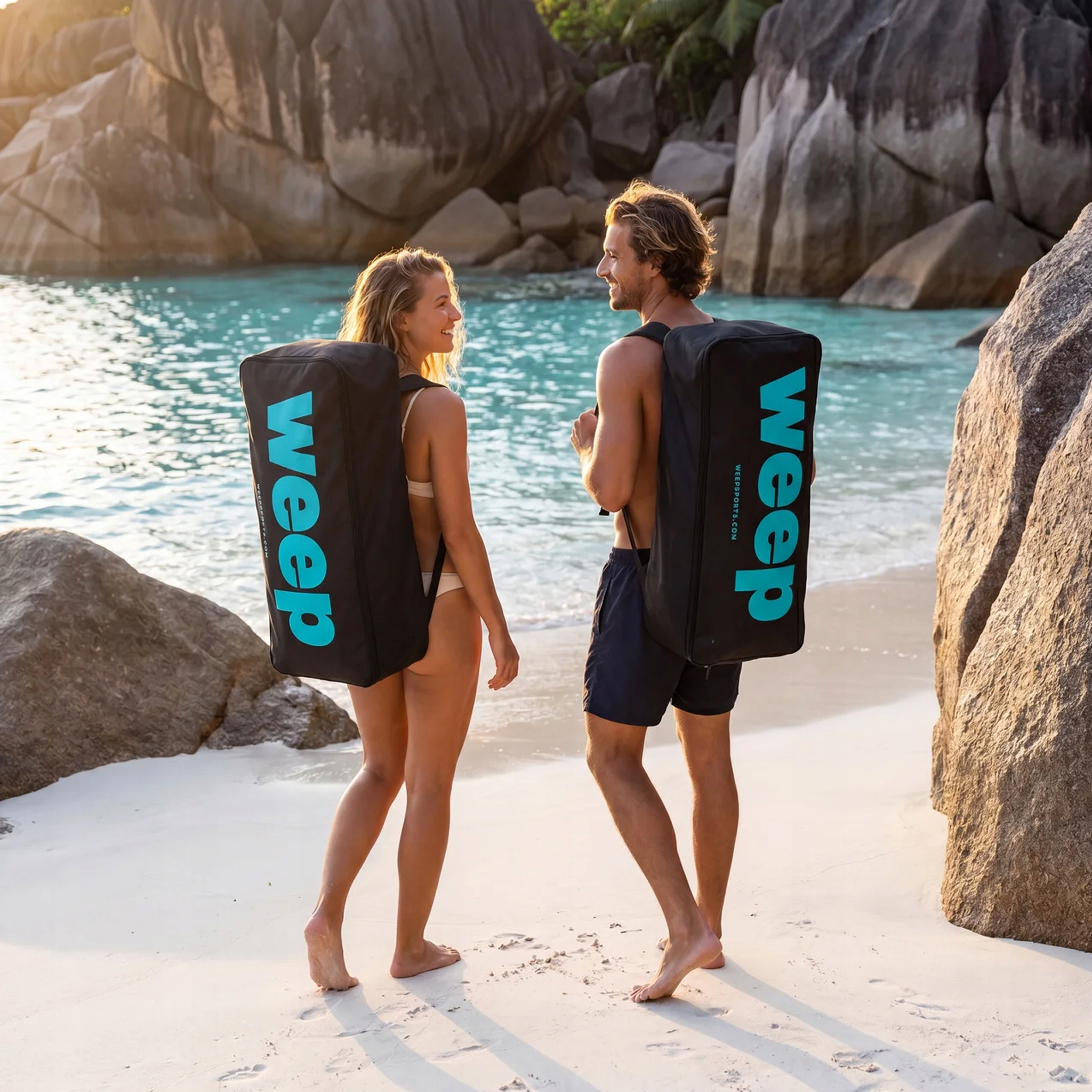 Mann und Frau mit schwarzen Taschen am Strand mit türkisfarbenem Wasser und Felsen.