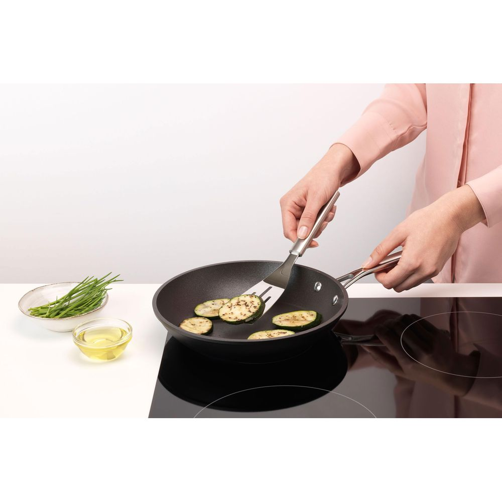 Zucchine fritte in padella, con erba cipollina e olio nelle vicinanze.