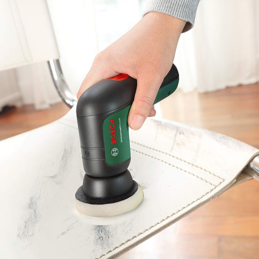 Bosch-Bürste reinigt weiße Lederfläche. Hand hält Werkzeug, Nahaufnahme.