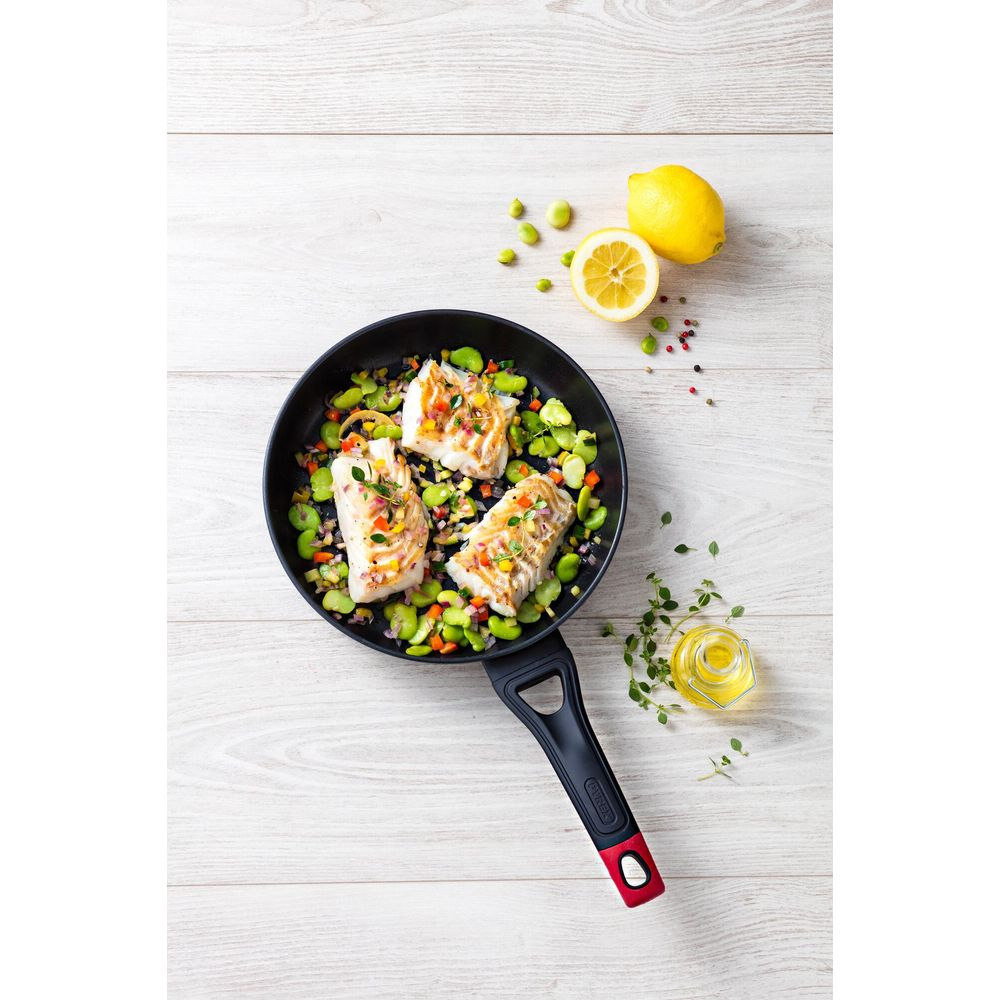 Gebratener Fisch mit Gemüse, Zitrone und Öl auf Holztisch.