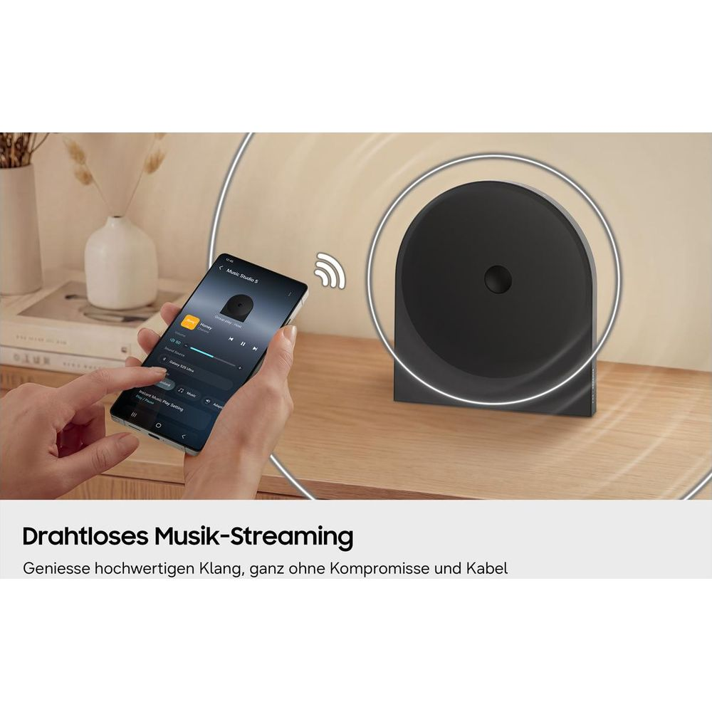 Eine Hand hält ein Smartphone mit Musik-App. Daneben steht ein schwarzer Lautsprecher.