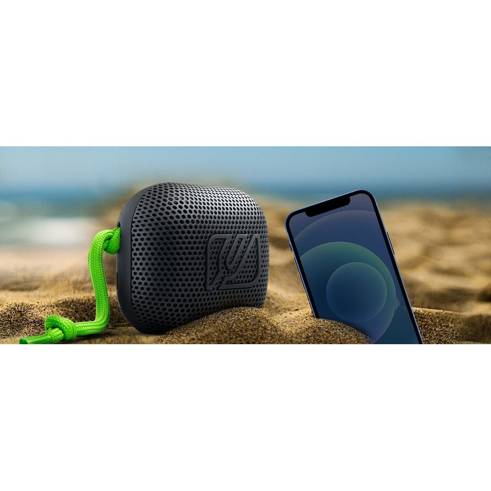 Uno speaker nero con corda verde e uno smartphone sulla sabbia in spiaggia.