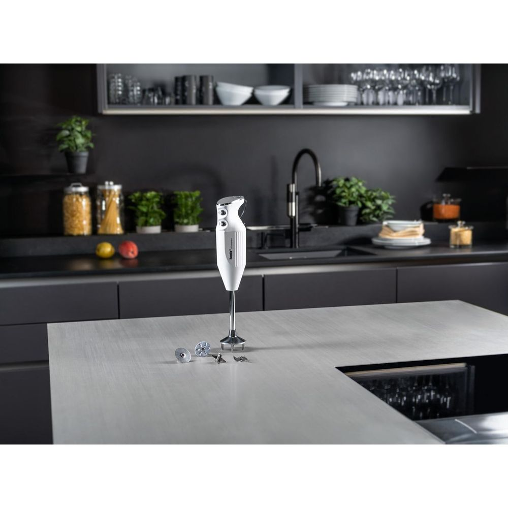 Un frullatore a immersione bianco si trova sul bancone della cucina accanto agli accessori.