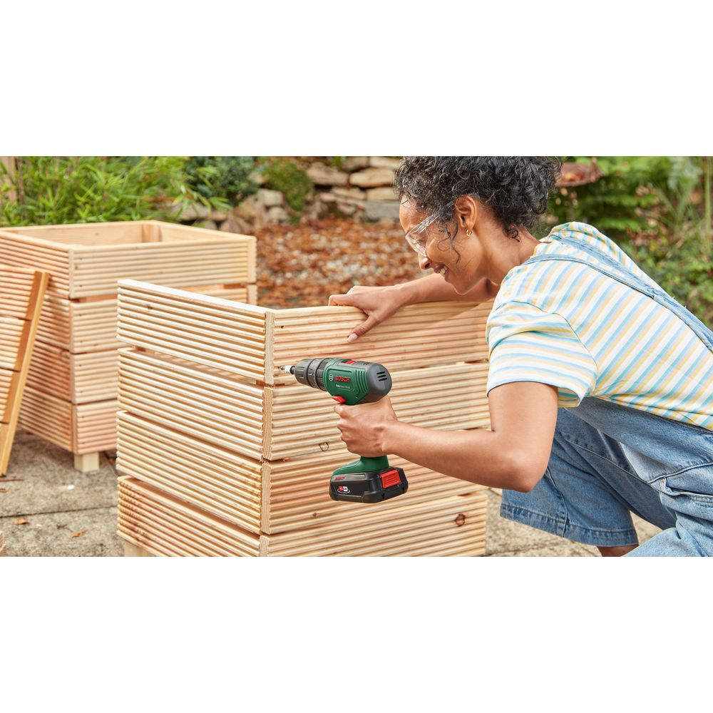 Una donna costruisce una fioriera in legno con un trapano a batteria in giardino.