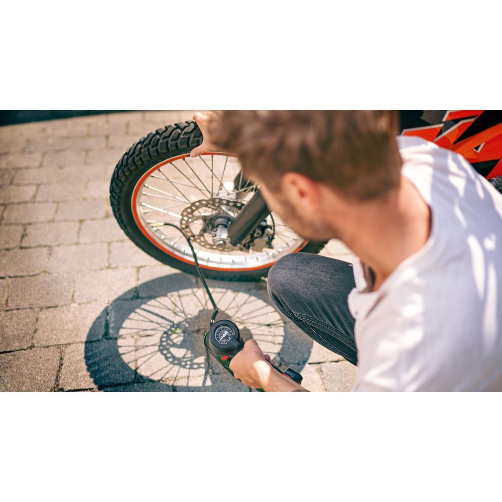 Mann pumpt Motorradreifen mit digitalem Manometer auf. Asphalt im Hintergrund.