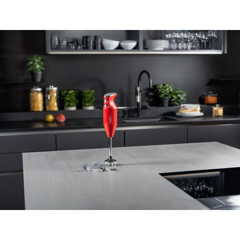 Frullatore a immersione rosso su piano di lavoro grigio con sfondo cucina. Lame vicine.