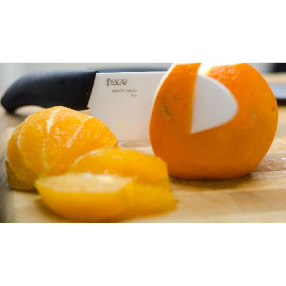 Ein Kyocera-Messer schält eine Orange auf einem Holzbrett.