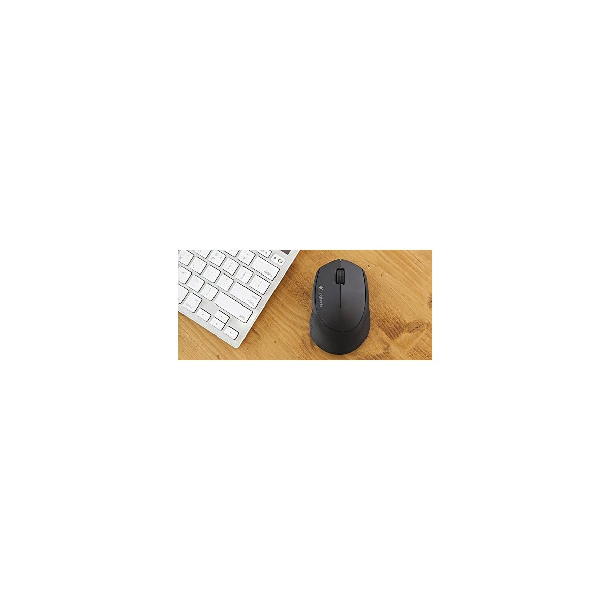 Un ratón negro descansa junto a un teclado blanco sobre un escritorio de madera.