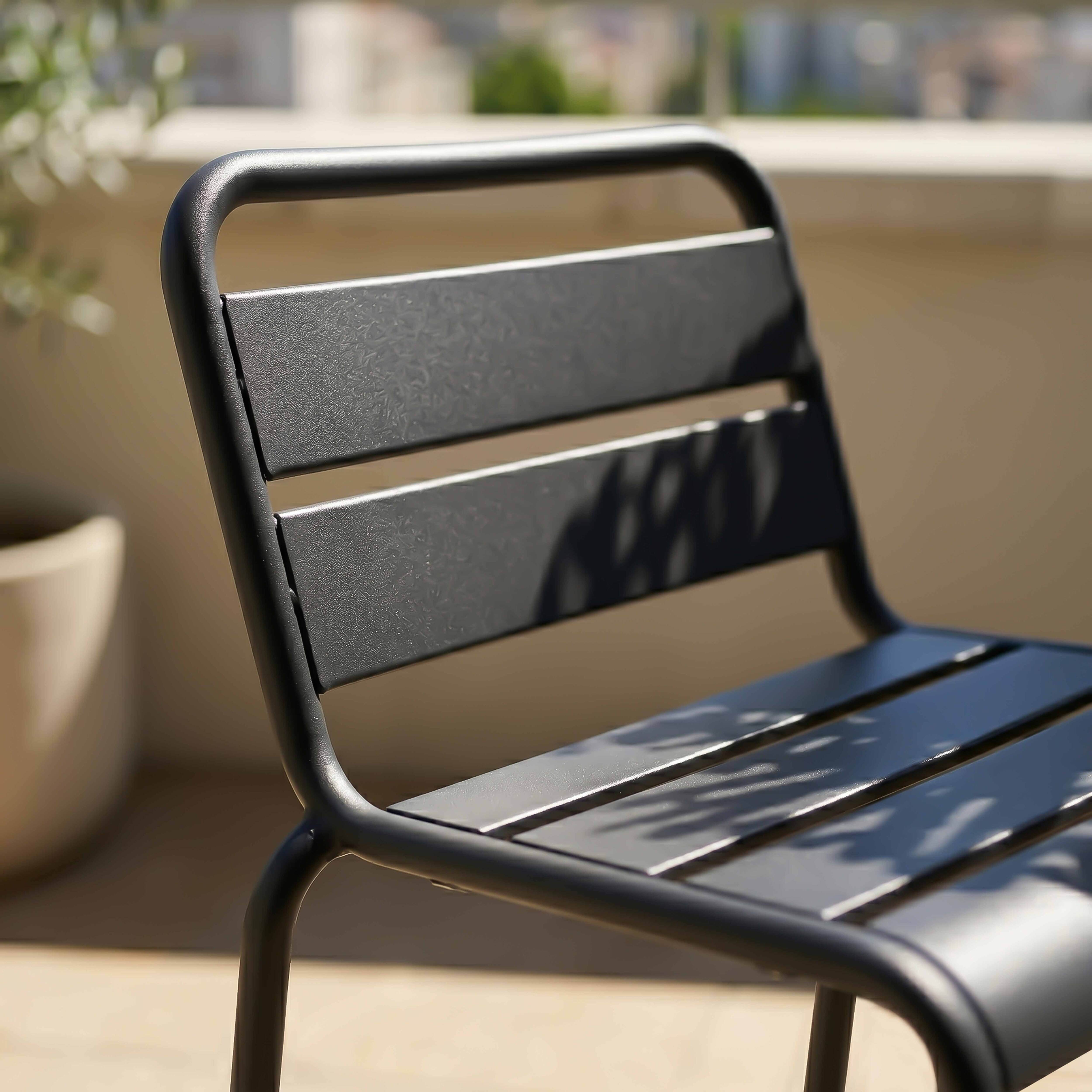 Ein anthrazitfarbener Metallstuhl mit Lamellen auf Sitz und Rücken steht auf einer Terrasse.