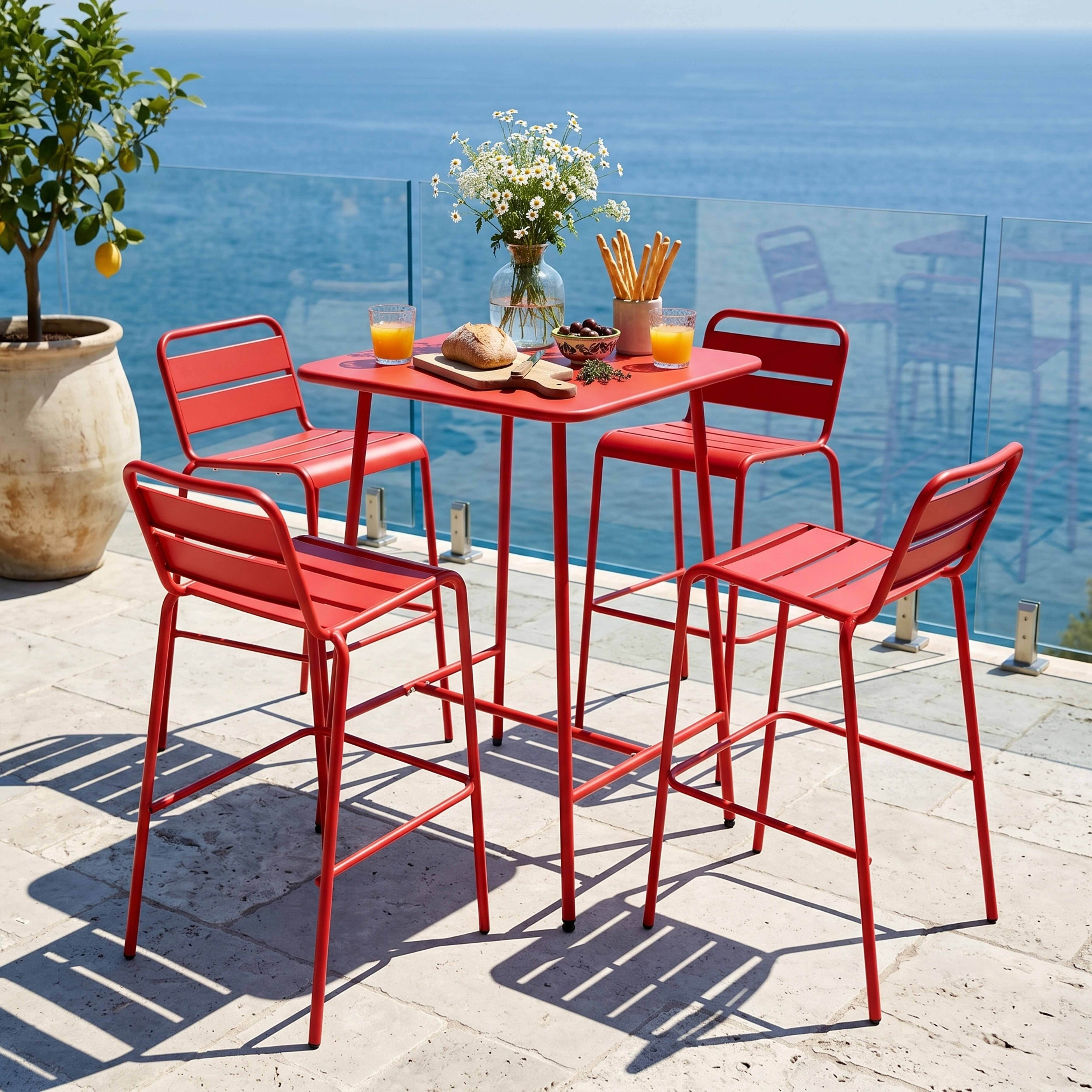 Roter Tisch mit vier Hockern am Meer, mit Orangengetränken, Brot und Blumen.