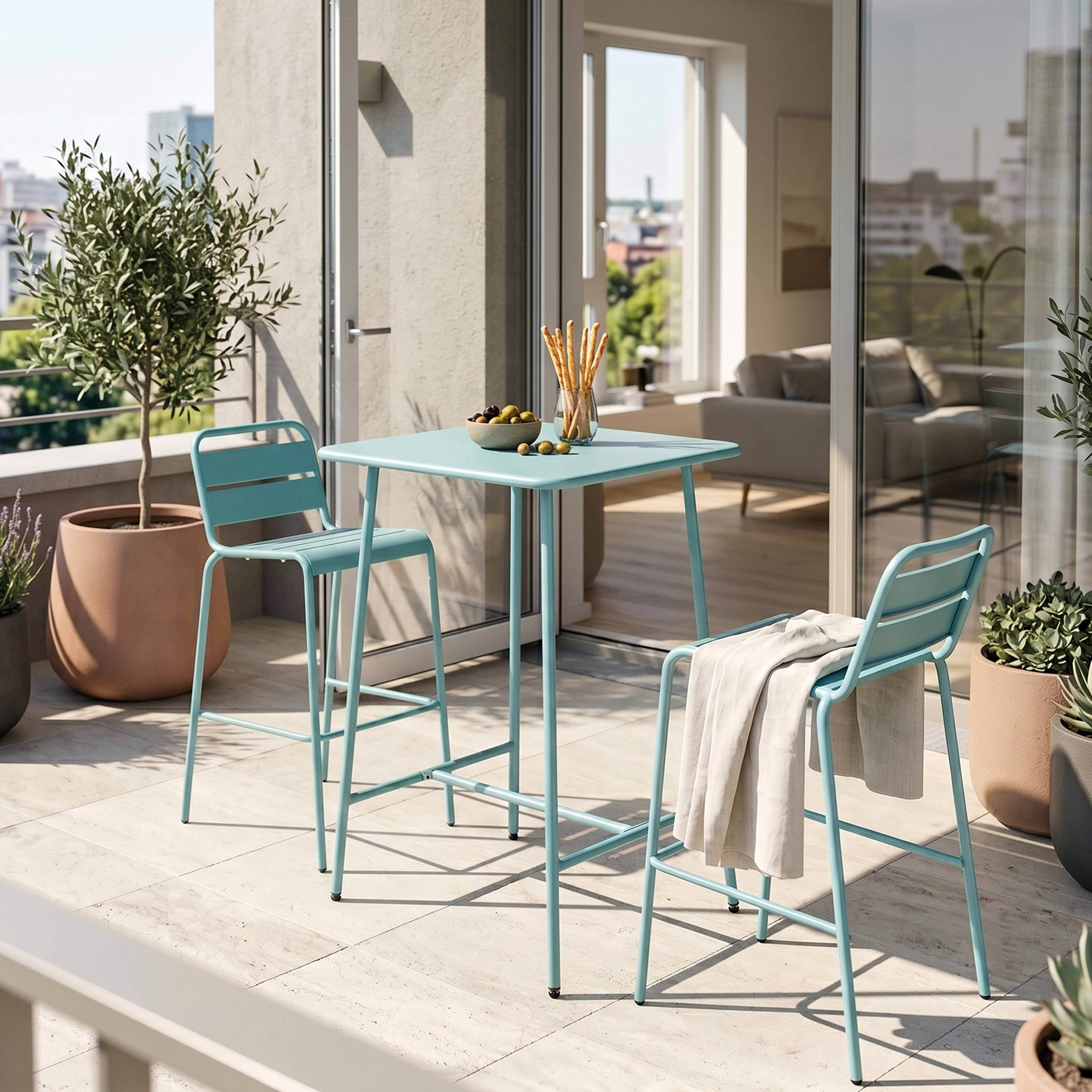 Ein türkisfarbener Tisch und zwei Hocker auf einer Terrasse mit Pflanzen und Stadtblick.