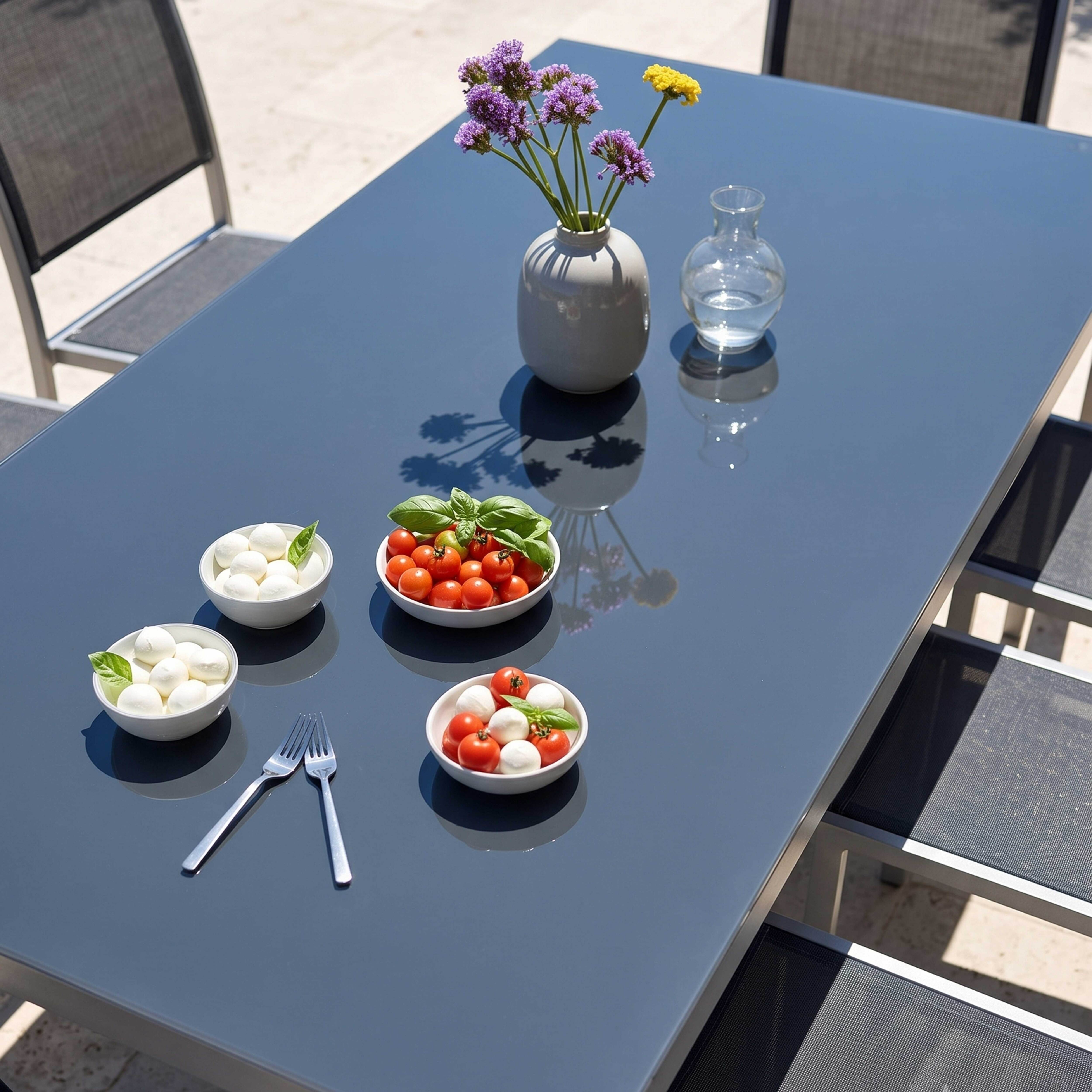 Ein grauer Tisch mit Mozzarella, Tomaten, Blumen und Gabeln im Freien.