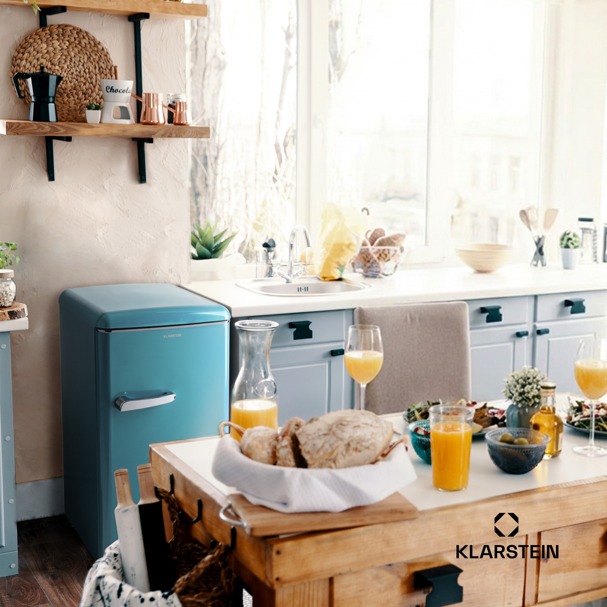 Eine blaue Küche mit Essecke: Kühlschrank, Spüle, Tisch mit Essen und Getränken.
