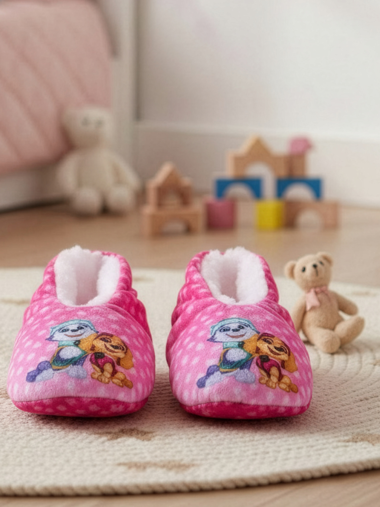 Zwei rosa Hausschuhe mit weißen Punkten und Paw Patrol-Motiv auf einem Teppich.
