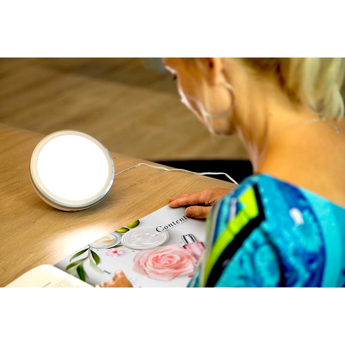 Eine Frau blickt auf eine helle Lampe und ein Magazin mit Rosenbildern.