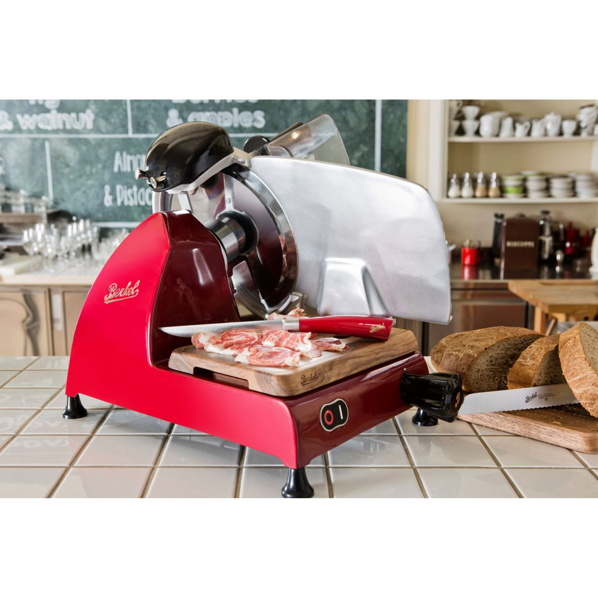 Una affettatrice Berkel rossa con prosciutto su un tagliere e pane affettato nelle vicinanze.