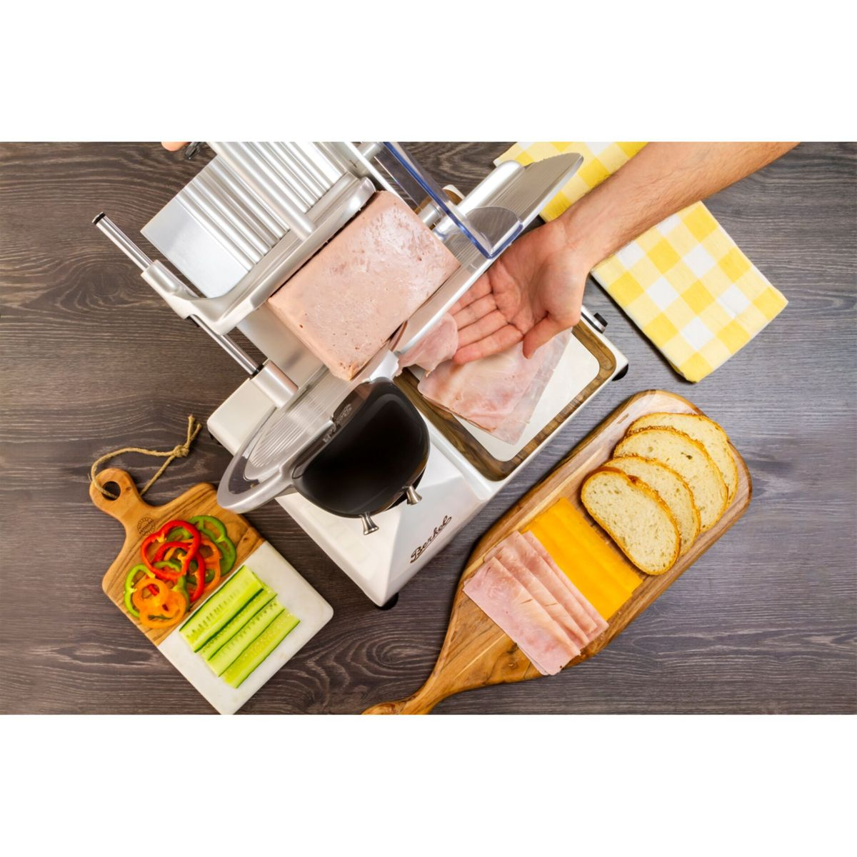 Una persona affetta prosciutto con un affettatore. Pane, formaggio e verdure sono vicini.