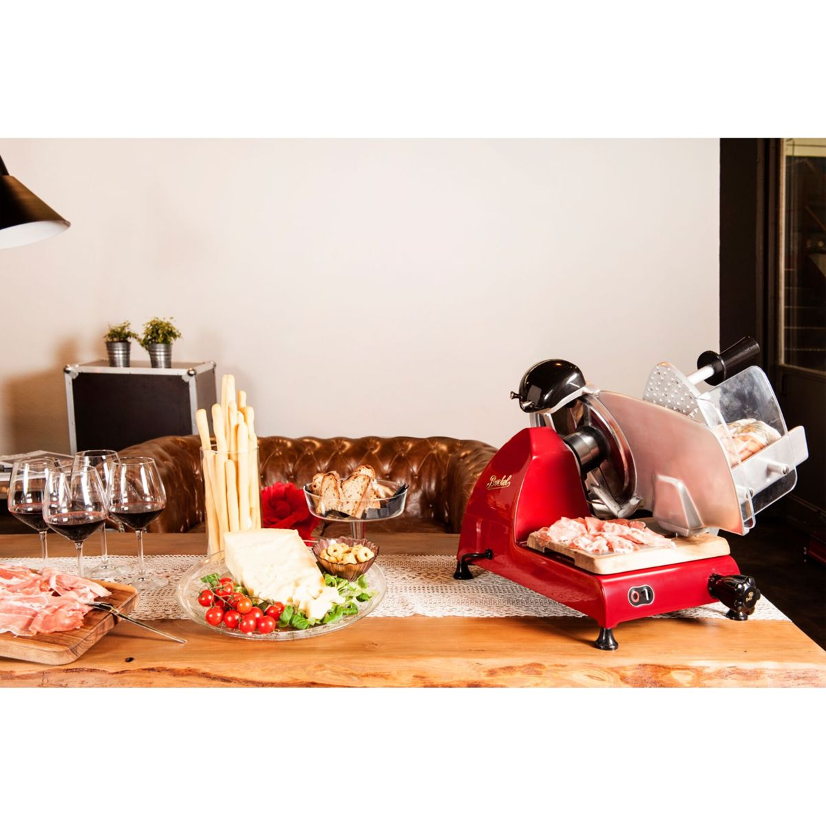 Una affettatrice rossa su un tavolo di legno con salumi, formaggio e pane.