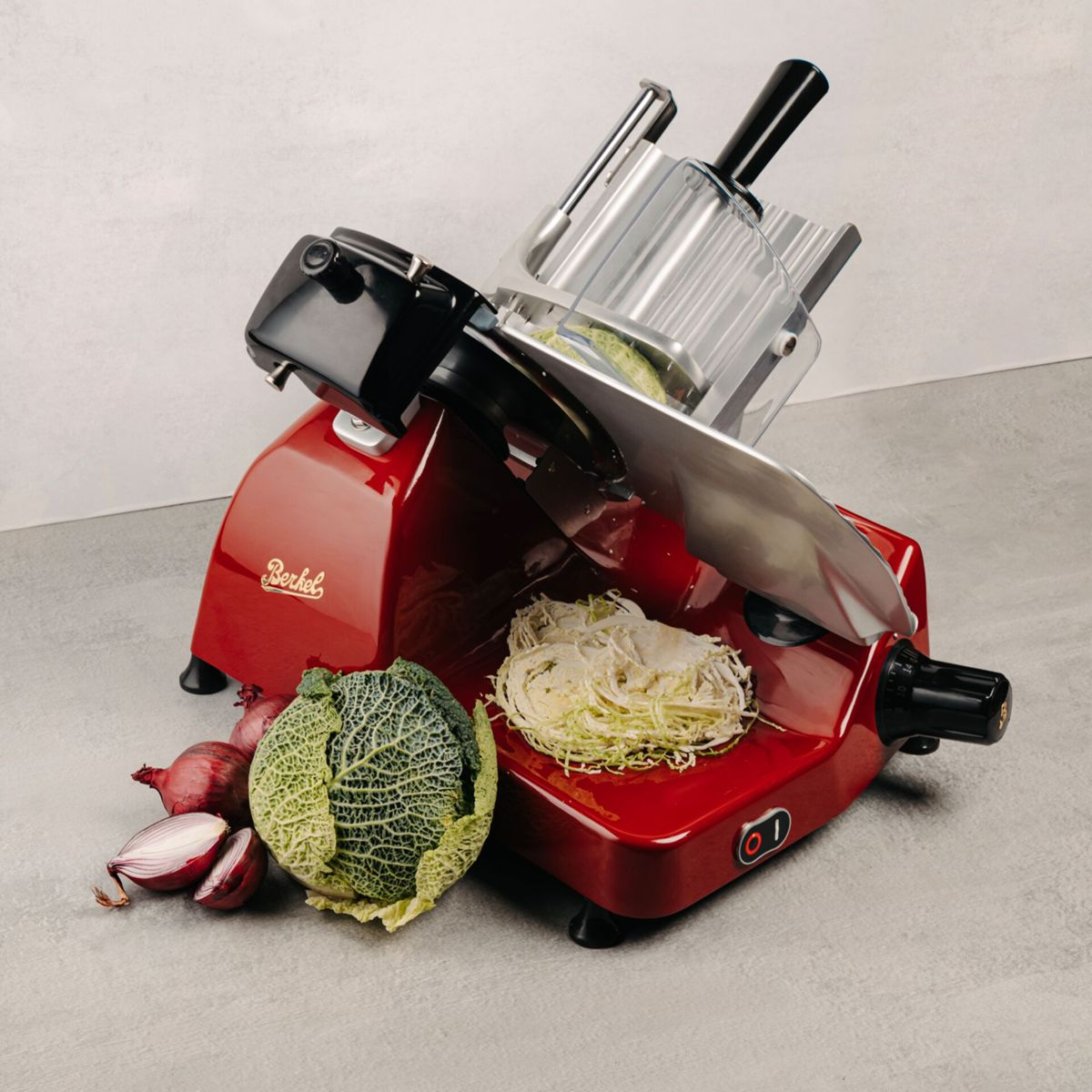 Affettatrice rossa con cavolo e cipolle accanto.