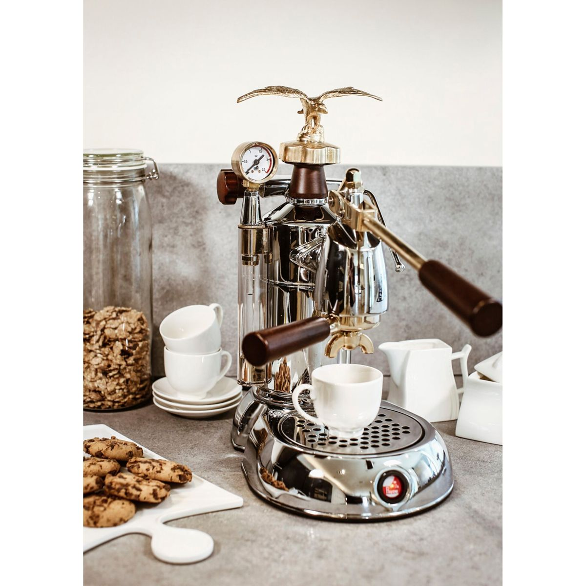 Błyszcząca maszyna do espresso z orłem, filiżankami, ciasteczkami i słoikiem.