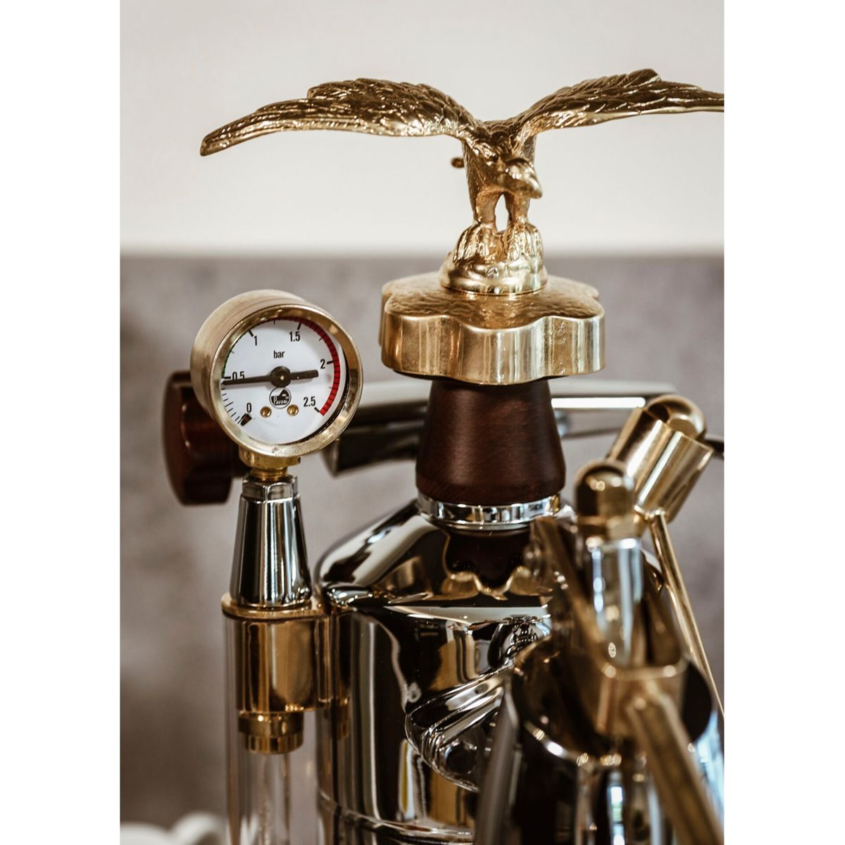Złota statua orła znajduje się na błyszczącej maszynie do espresso z mosiężnymi detalami i manometrem.