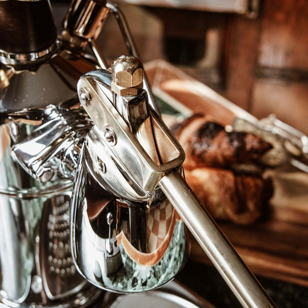 Zbliżenie błyszczącej maszyny do espresso ze złotą śrubą i dźwignią.