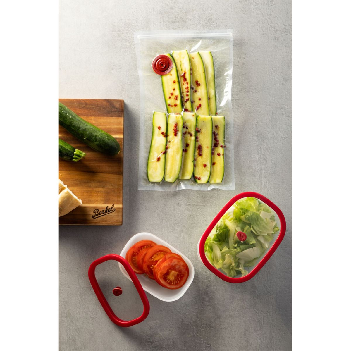 Zucchini-Sticks in Vakuumbeutel, Tomatenscheiben und Salat auf Steinplatte.