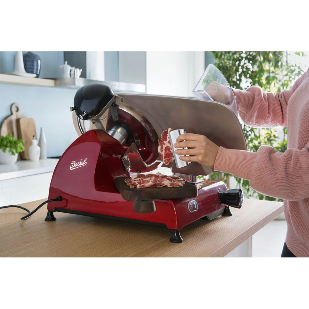 Ein roter Berkel-Schneider wird von einer Person im rosa Pullover zum Schneiden von Fleisch verwendet.