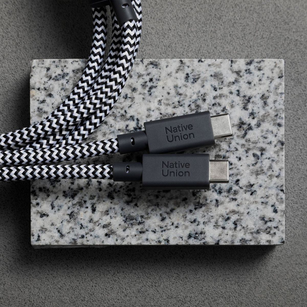Zwei USB-C-Kabel mit schwarz-weißer Zickzackmusterung liegen auf Granit.