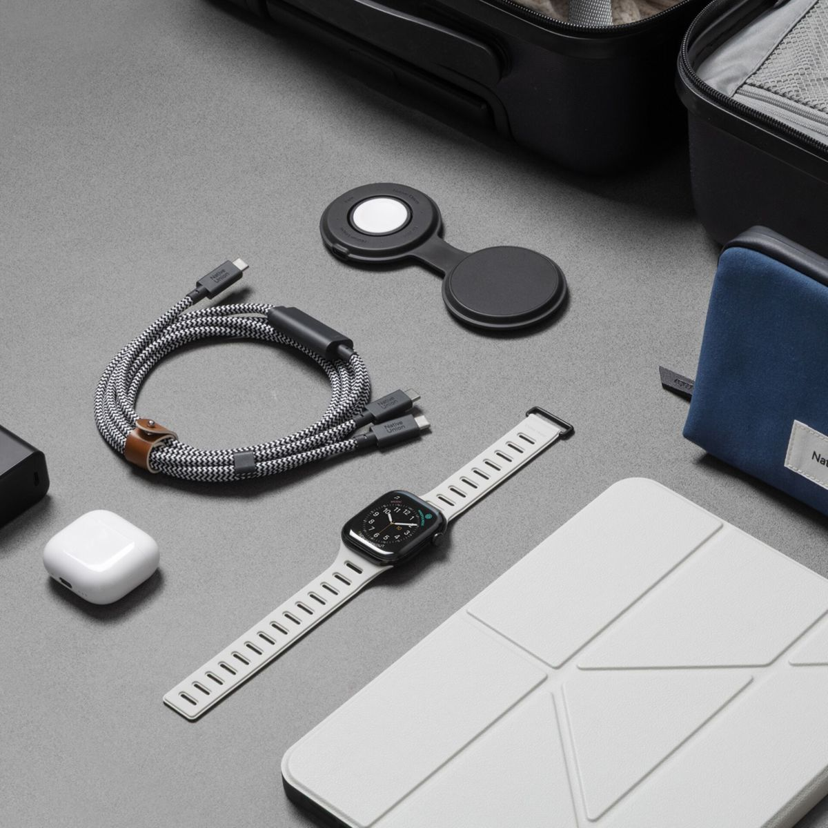 Gadgets auf grauer Oberfläche: Kabel, Uhr, Ohrhörer, Ladegerät, Hülle, Tasche.