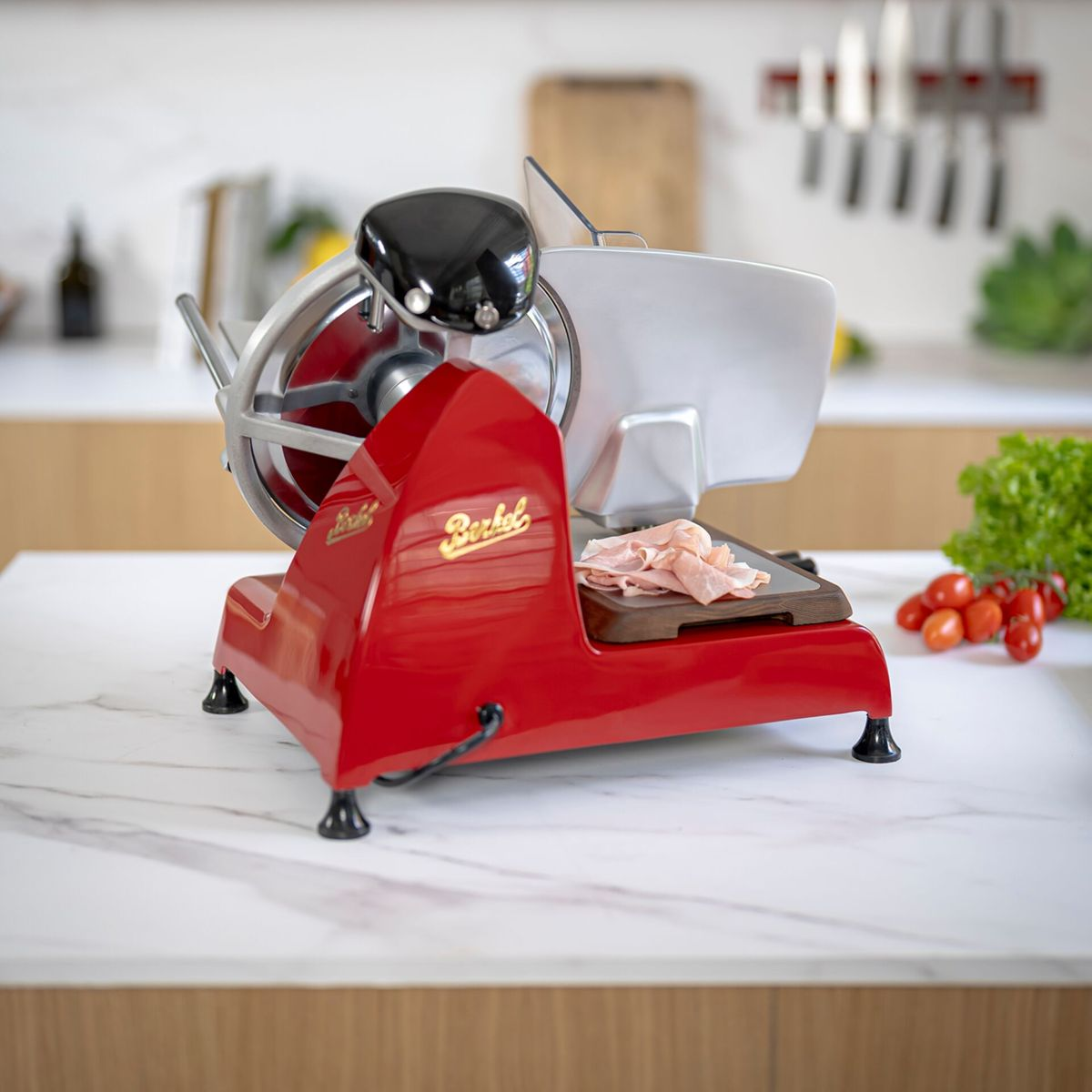 A red Berkel slicer with slices of cold cuts on a wooden board.