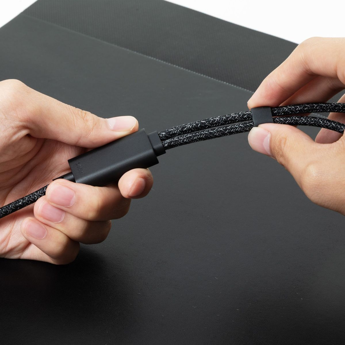 Hände halten ein schwarzes geflochtenes Kabel mit schwarzem Stecker und schwarzem Kabelbinder.