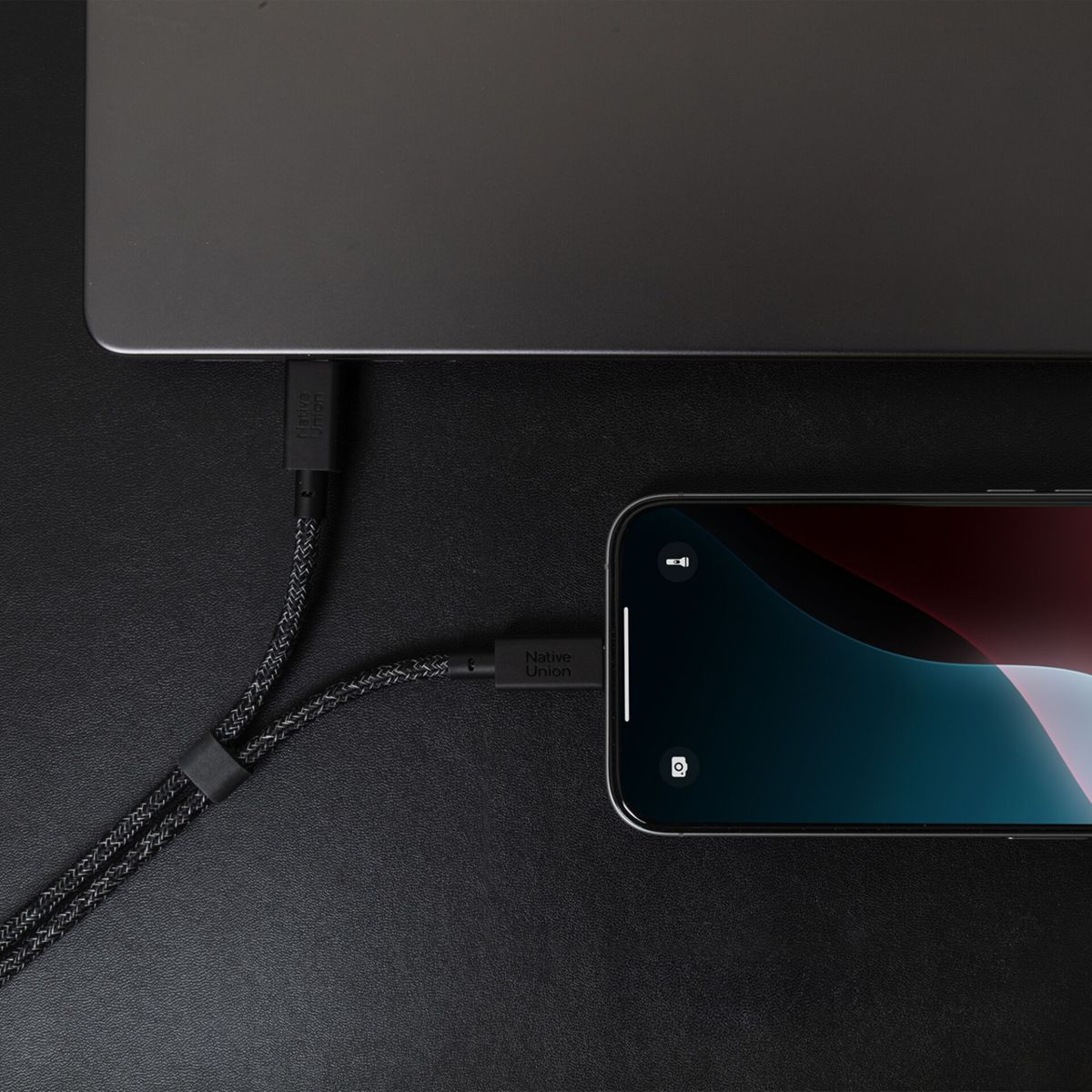 Ein schwarzes geflochtenes Kabel verbindet einen Laptop mit einem Smartphone und lädt es auf.
