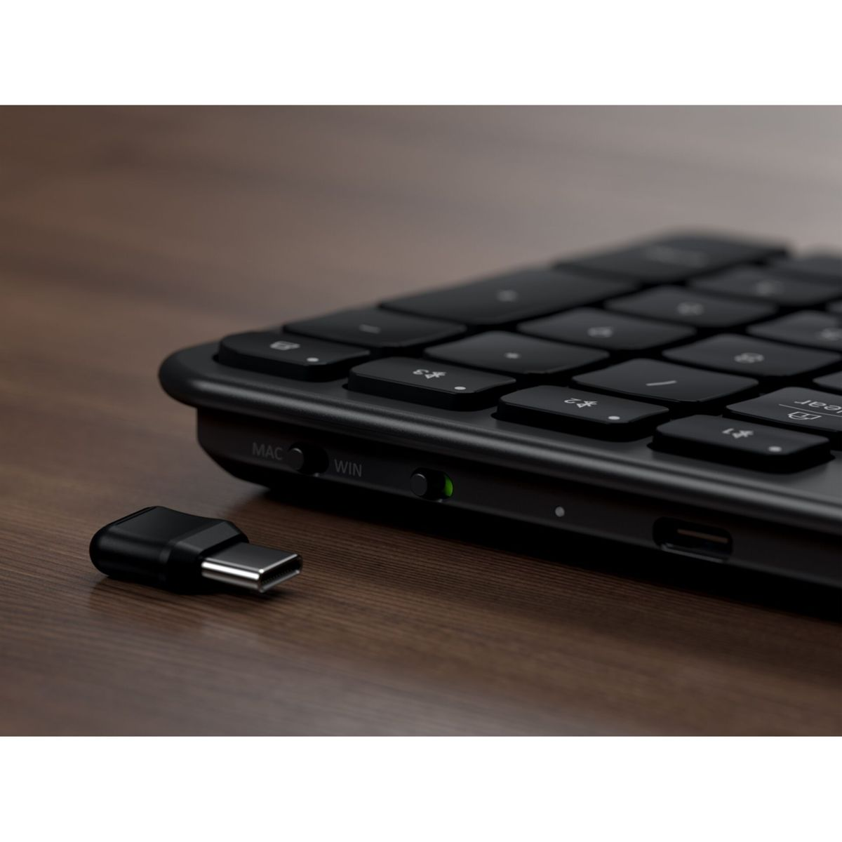 Ein schwarzer USB-C-Dongle liegt neben einer schwarzen Tastatur auf einem Holztisch.