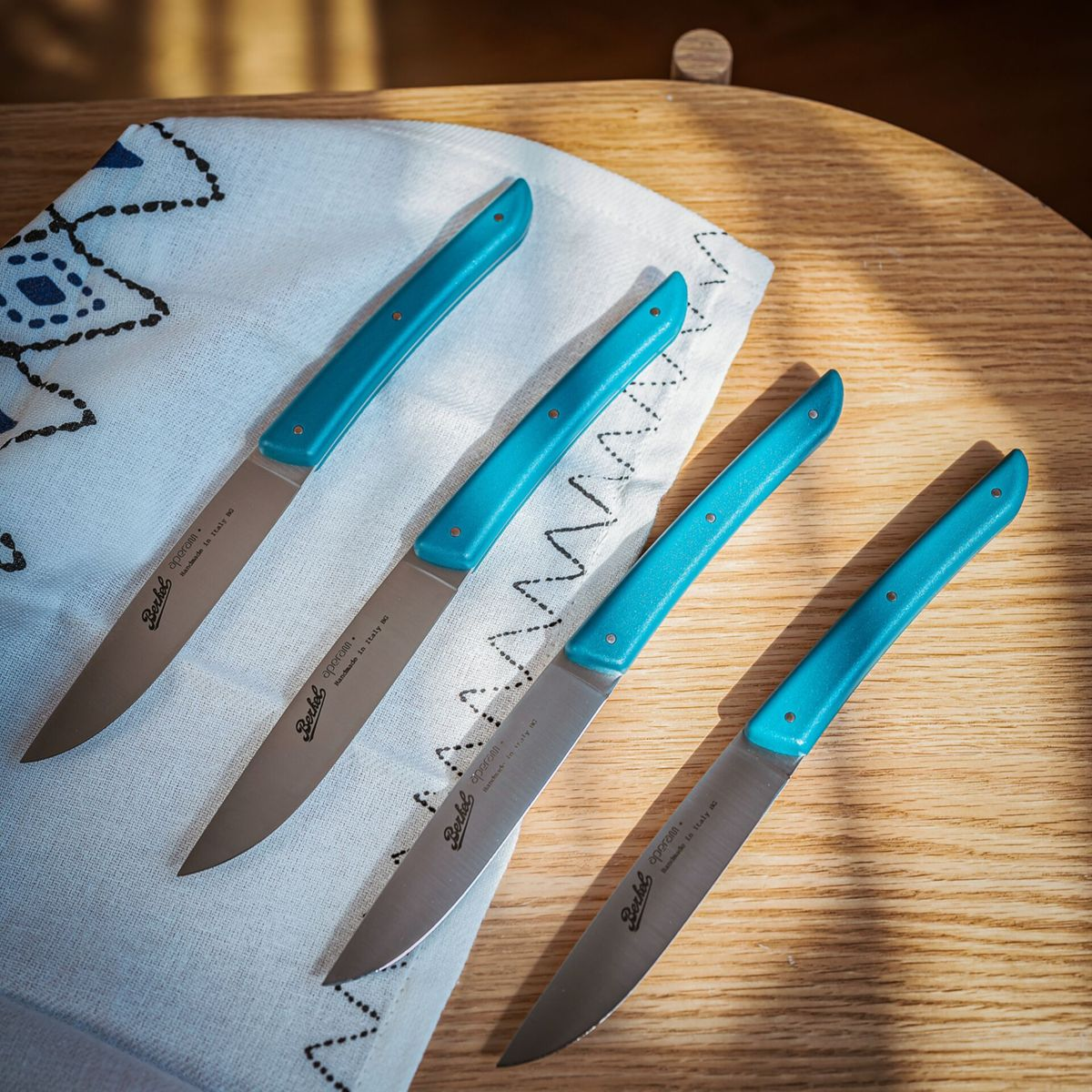 Vier messen met turquoise handvatten op een wit doek met blauw patroon.