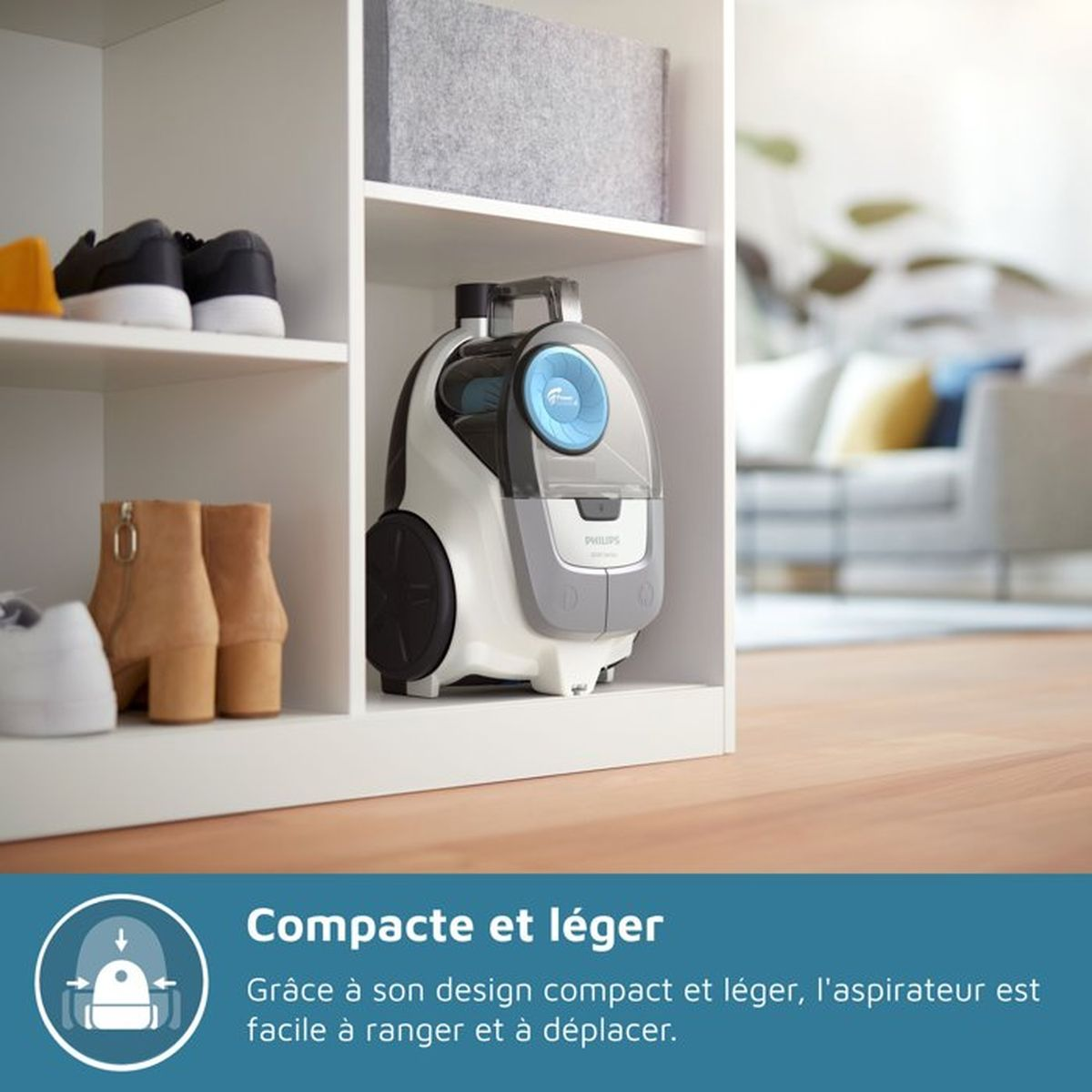 Een compacte wit-grijze Philips stofzuiger staat op een plank naast schoenen.